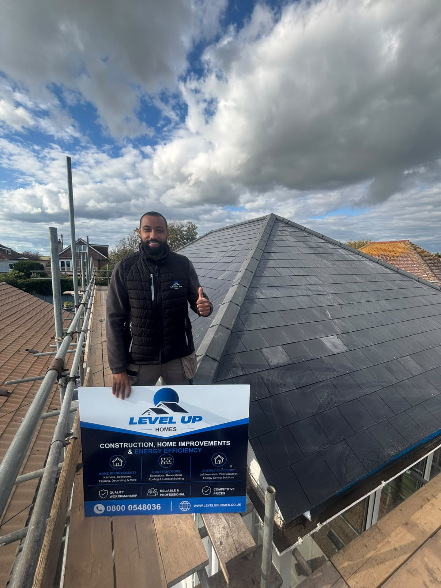 Level Up Homes team member on a finished slate roof, holding a Level Up Homes signboard